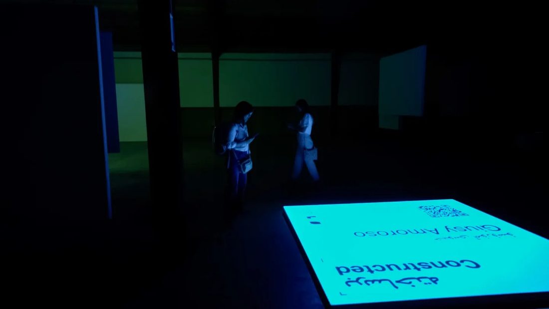 Visitors reading the Constructed floor plate in a darkened gallery